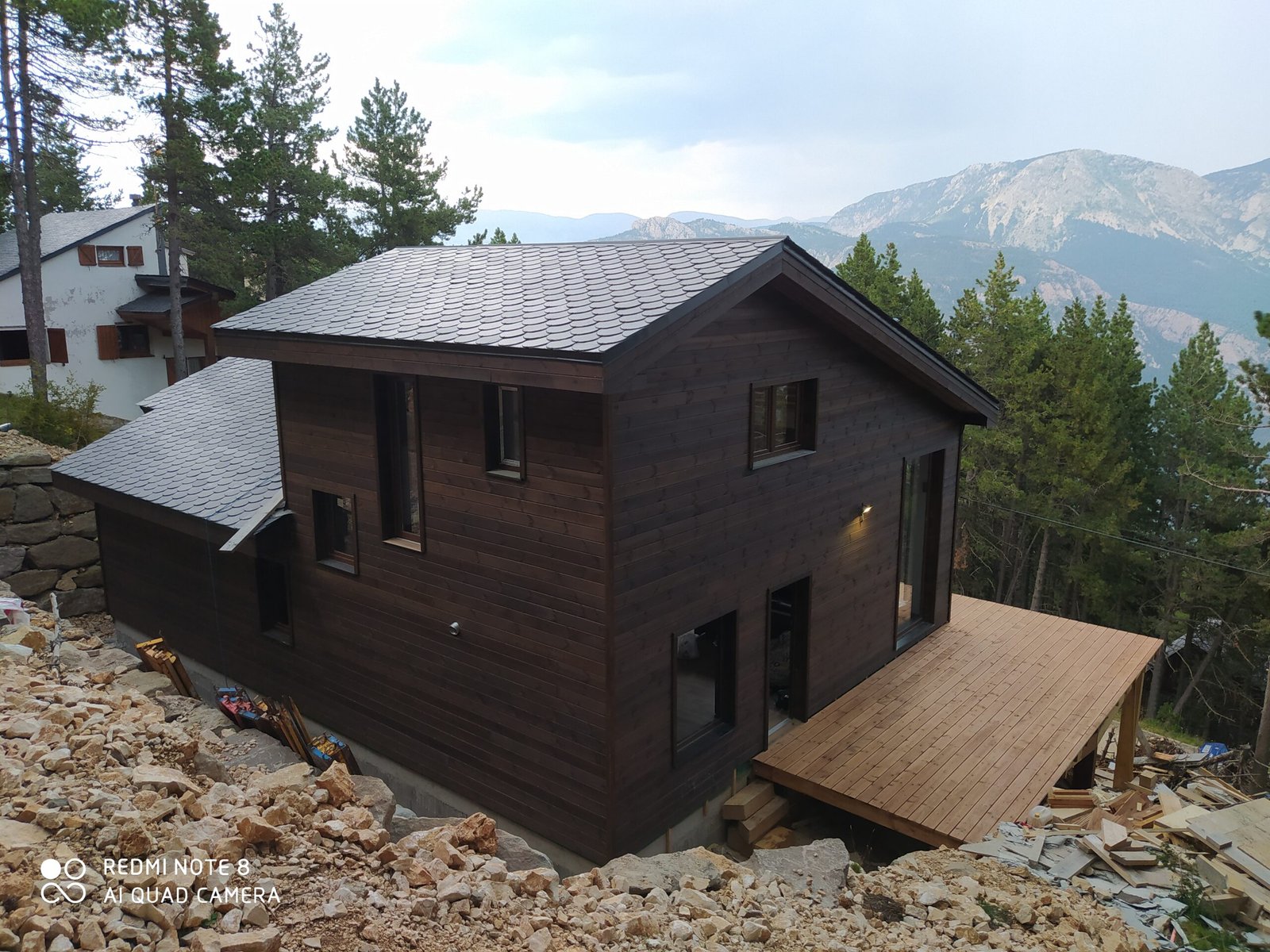 Casa prefabricada con acabados de madera con tejado a dos aguas de pizarra, rodeada de árboles en la montaña.