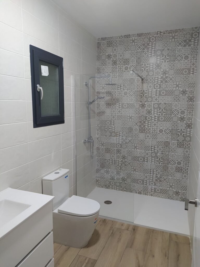 Baño completo con ducha y mampara en casa prefabricada con suelo efecto madera