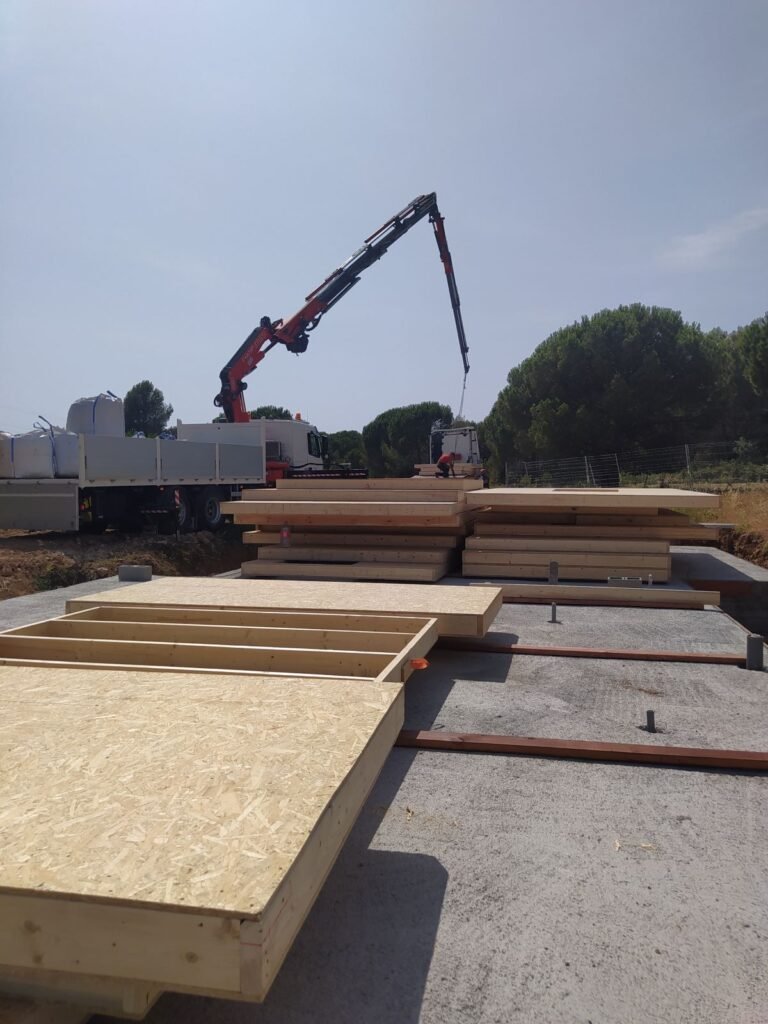 Paneles prefabricados de madera preparados para montaje de casa prefabricada en Port del Comte con grúa en obra