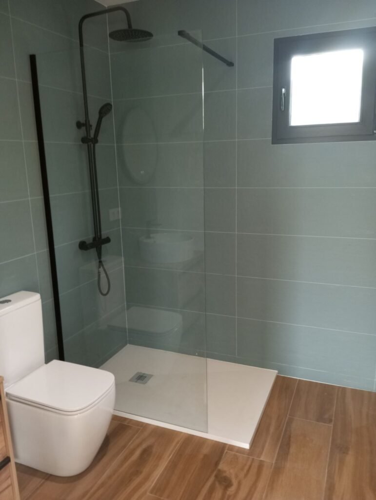 Baño moderno con plato de ducha, mampara de cristal, grifería negra y azulejos verdes