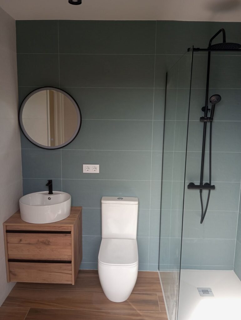 Baño moderno con ducha y mampara de cristal, mueble de madera y azulejos en tono verde