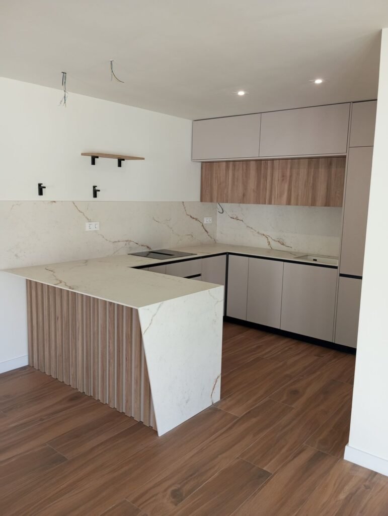 Cocina moderna con isla central, encimera efecto mármol y muebles blancos con acabado madera