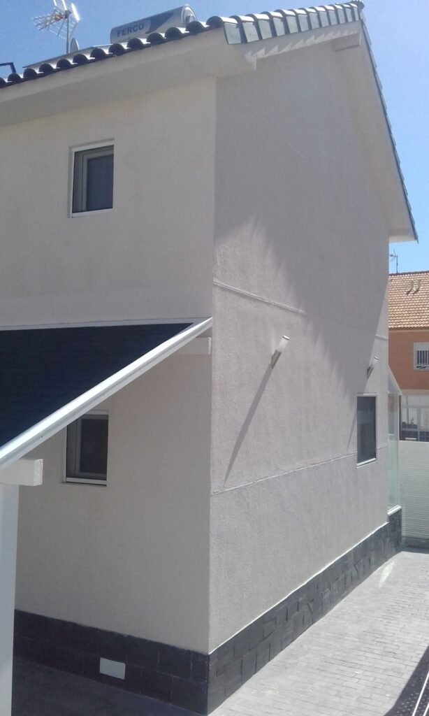 Vista lateral de casa prefabricada de dos plantas terminada con aislamiento exterior y cubierta inclinada