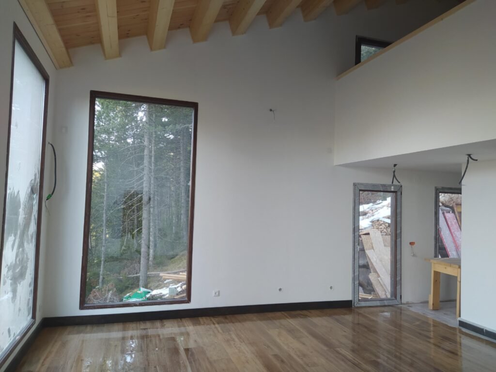 Salón de doble altura con grandes ventanales en casa prefabricada de madera en Port del Comte